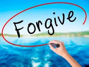 image of hand writing the word forgive over the ocean