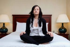 A woman in work clothes sitting on bed in meditative position.